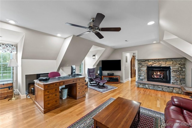 interior space with light wood-type flooring, a stone fireplace, ceiling fan, and lofted ceiling