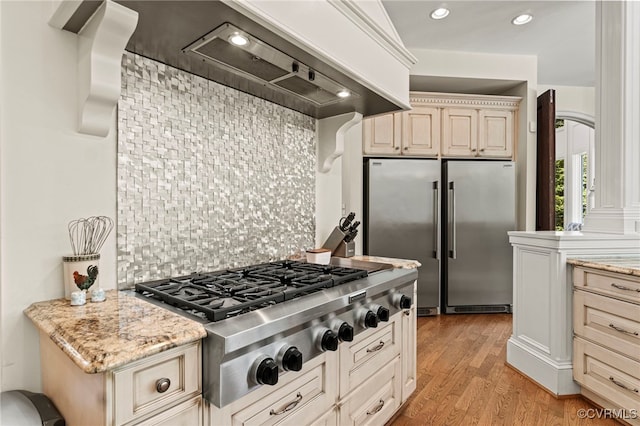 kitchen featuring stainless steel appliances, light hardwood / wood-style floors, tasteful backsplash, light stone countertops, and cream cabinetry