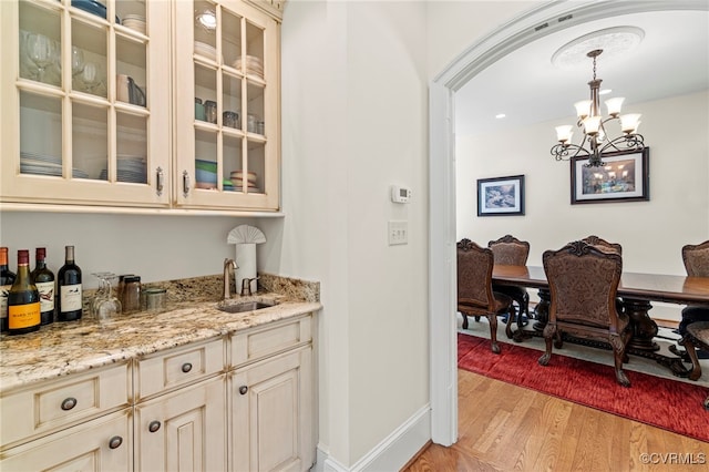 bar featuring light hardwood / wood-style floors, cream cabinets, sink, a chandelier, and decorative light fixtures