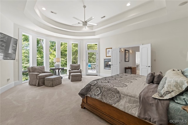 carpeted bedroom featuring ceiling fan, multiple windows, access to exterior, and a tray ceiling