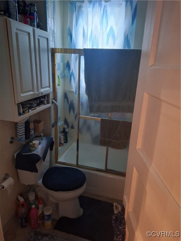 bathroom featuring toilet, shower / bath combination with glass door, and backsplash