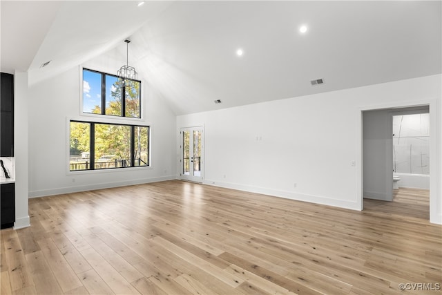 unfurnished living room with high vaulted ceiling, light wood-style flooring, visible vents, baseboards, and an inviting chandelier