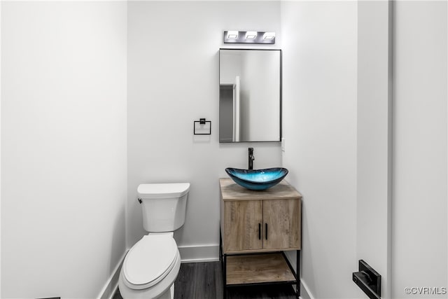 half bathroom with toilet, baseboards, wood finished floors, and vanity