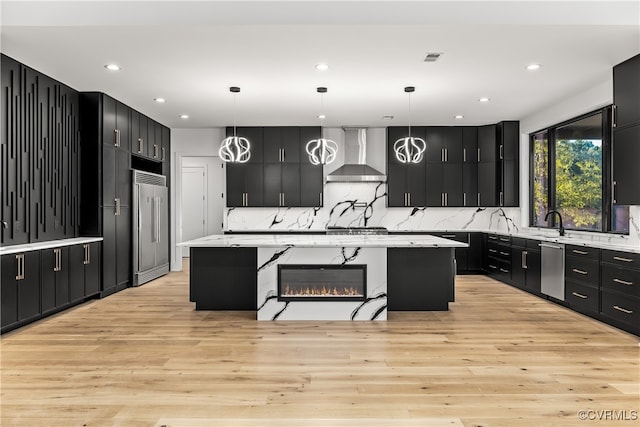 kitchen with wall chimney range hood, a spacious island, stainless steel appliances, and dark cabinets