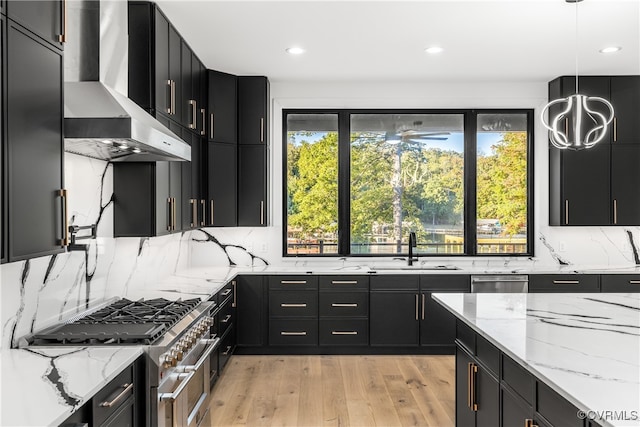 kitchen with decorative light fixtures, appliances with stainless steel finishes, a sink, wall chimney range hood, and dark cabinetry