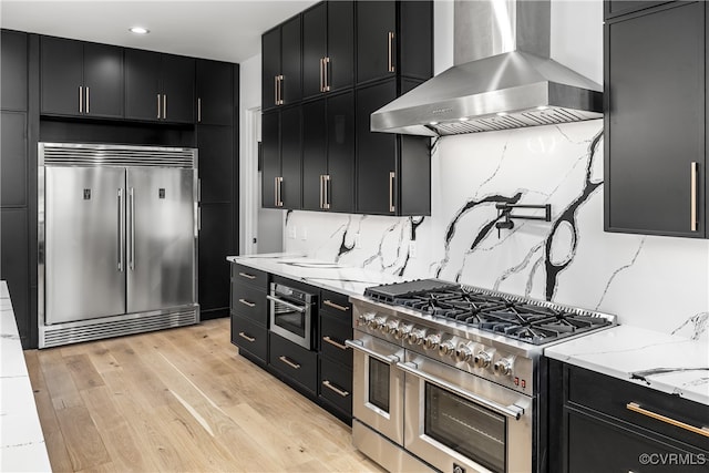 kitchen featuring wall chimney exhaust hood, premium appliances, and dark cabinets