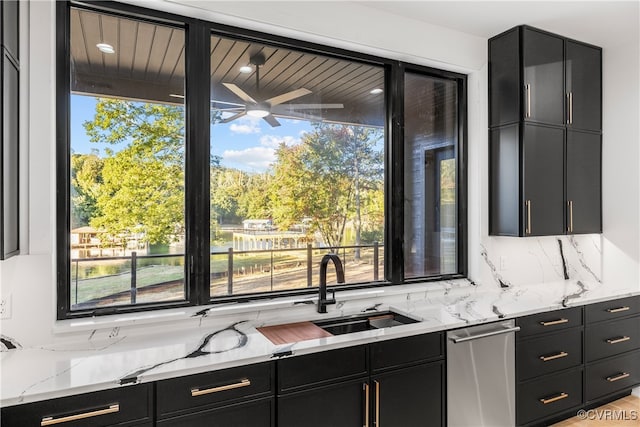 kitchen with light stone counters, a sink, stainless steel dishwasher, dark cabinetry, and backsplash