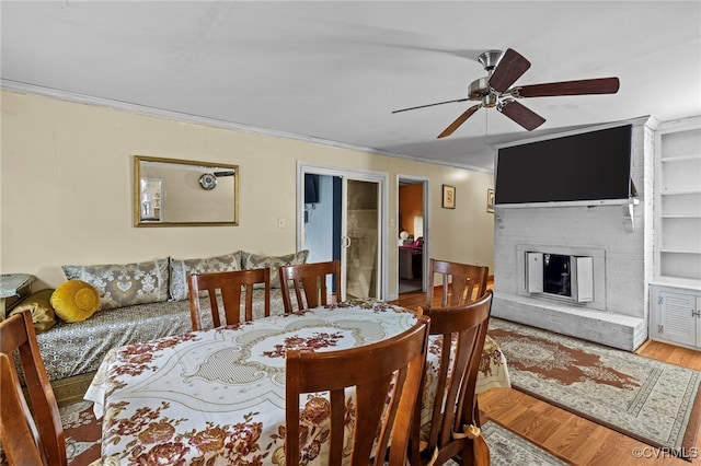 dining area with built in shelves, ornamental molding, ceiling fan, hardwood / wood-style floors, and a fireplace