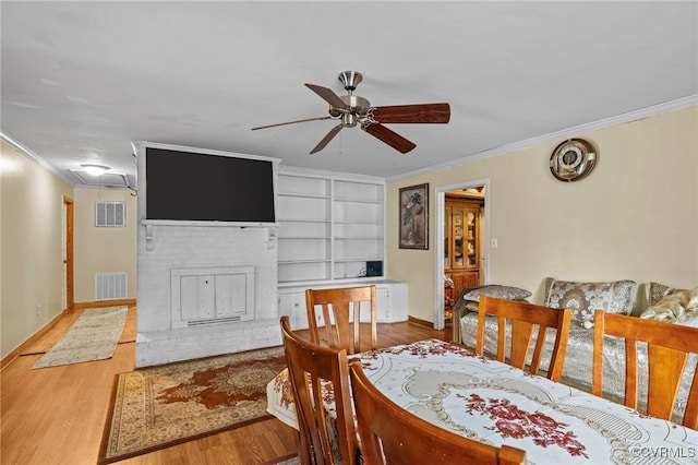 dining area with a brick fireplace, wood-type flooring, built in features, and crown molding