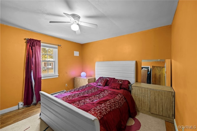 bedroom with light hardwood / wood-style floors, ceiling fan, and baseboard heating