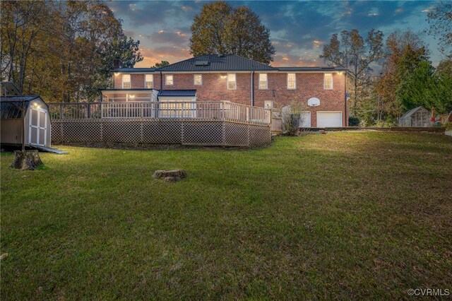 back house at dusk featuring a storage unit, a garage, a yard, and a wooden deck