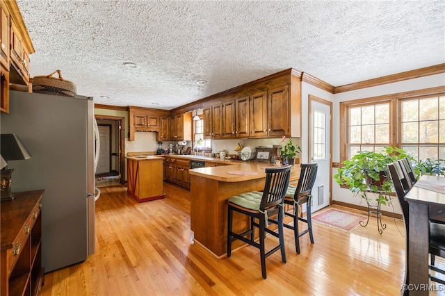 kitchen with kitchen peninsula, stainless steel fridge, light wood-type flooring, ornamental molding, and a breakfast bar area