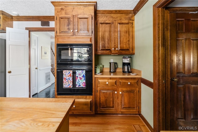 kitchen with a textured ceiling, crown molding, black appliances, hardwood / wood-style flooring, and butcher block counters