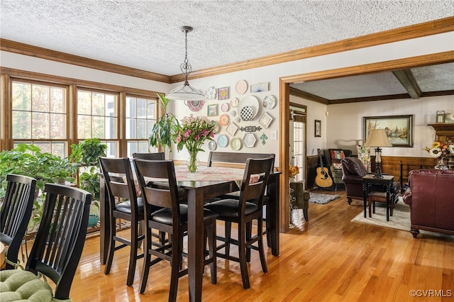 dining room featuring crown molding, light wood-type flooring, and a textured ceiling