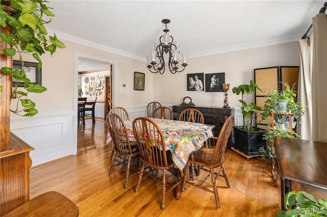 dining area with a textured ceiling, an inviting chandelier, light hardwood / wood-style flooring, and ornamental molding