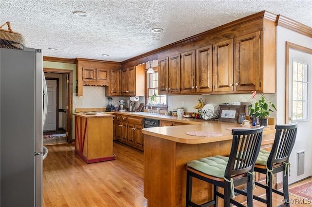 kitchen featuring a breakfast bar, stainless steel fridge, ornamental molding, light hardwood / wood-style floors, and kitchen peninsula