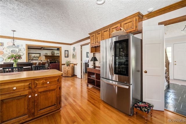 kitchen with pendant lighting, crown molding, stainless steel fridge, a textured ceiling, and light hardwood / wood-style floors