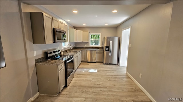 kitchen with dark stone countertops, stainless steel appliances, sink, and light wood-type flooring