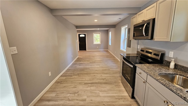 kitchen with sink, stainless steel appliances, light wood-type flooring, and dark stone counters