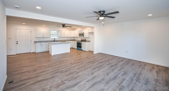 kitchen with a kitchen island, appliances with stainless steel finishes, white cabinetry, sink, and light stone countertops