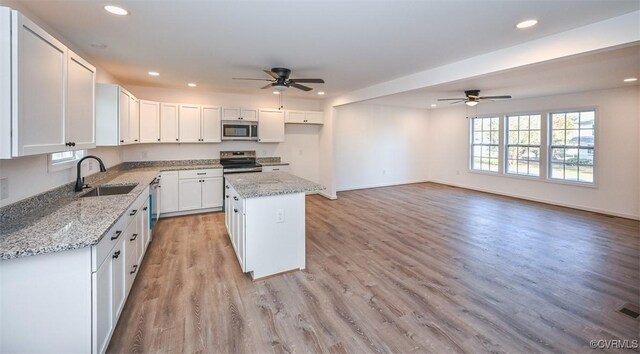 kitchen featuring sink, stainless steel appliances, light stone counters, white cabinets, and a kitchen island