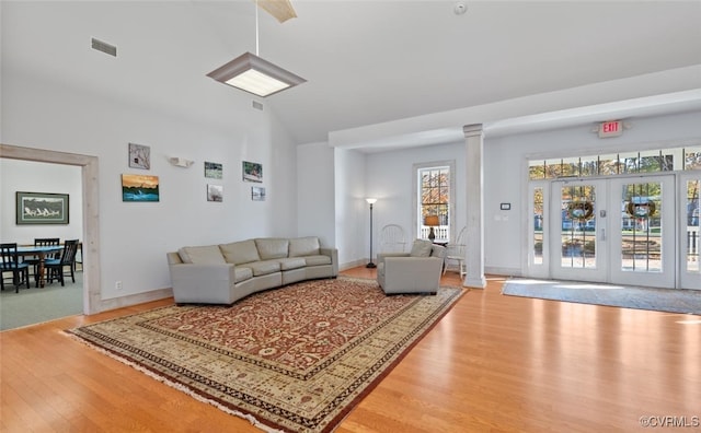 living room featuring a wealth of natural light, french doors, light wood-type flooring, and decorative columns