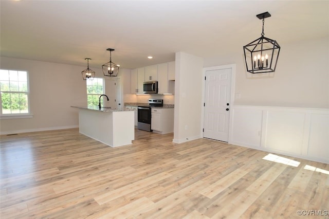 kitchen featuring appliances with stainless steel finishes, decorative light fixtures, white cabinets, light hardwood / wood-style flooring, and a kitchen island with sink