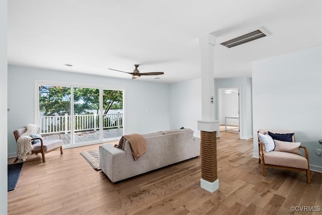 living area featuring light wood-style floors, visible vents, ornate columns, and a ceiling fan