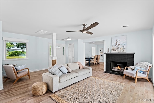 living room featuring light hardwood / wood-style floors, decorative columns, a fireplace, and ceiling fan