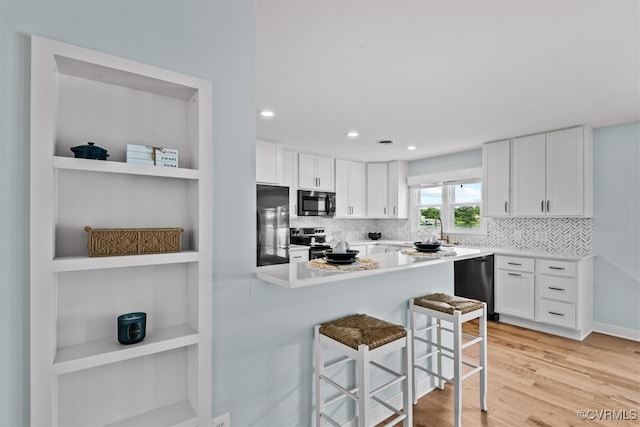 kitchen with decorative backsplash, white cabinets, a kitchen breakfast bar, light wood-type flooring, and stainless steel appliances