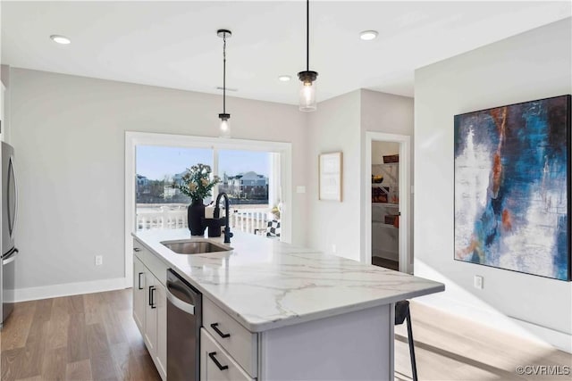 kitchen featuring an island with sink, stainless steel appliances, pendant lighting, sink, and white cabinetry