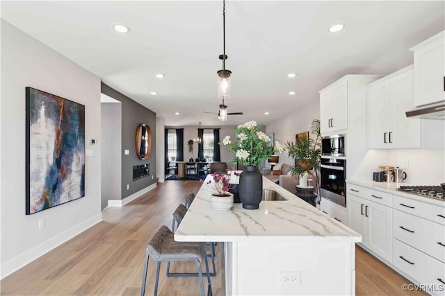 kitchen with appliances with stainless steel finishes, decorative light fixtures, a kitchen island with sink, and white cabinets