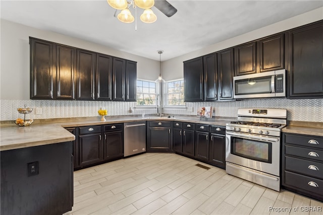 kitchen featuring decorative backsplash, appliances with stainless steel finishes, sink, pendant lighting, and butcher block countertops