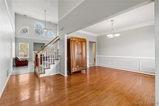 foyer entrance featuring crown molding, wood-type flooring, and ceiling fan with notable chandelier