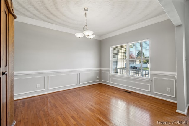 spare room featuring an inviting chandelier, crown molding, and hardwood / wood-style floors