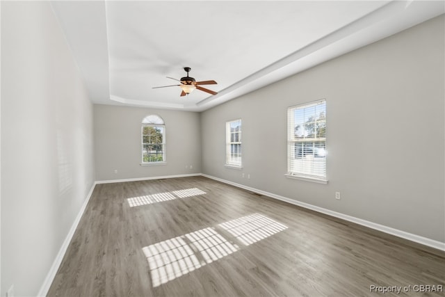 empty room featuring hardwood / wood-style flooring, a raised ceiling, and ceiling fan