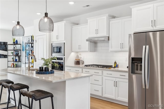 kitchen featuring light stone countertops, white cabinetry, stainless steel appliances, and a kitchen island with sink