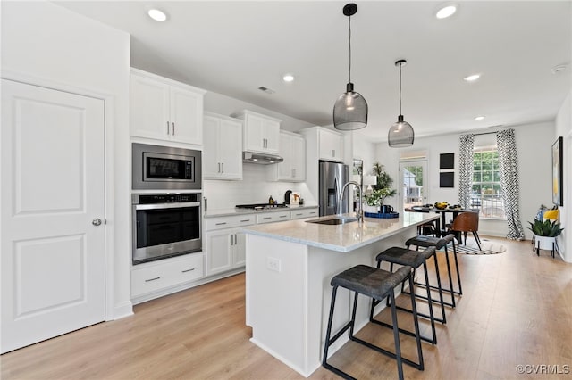 kitchen with a center island with sink, sink, appliances with stainless steel finishes, decorative light fixtures, and white cabinetry