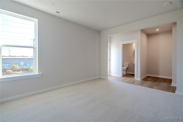 unfurnished bedroom with ensuite bath and light wood-type flooring