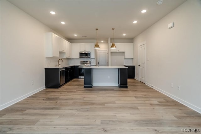 kitchen with a center island, white cabinets, sink, appliances with stainless steel finishes, and decorative light fixtures