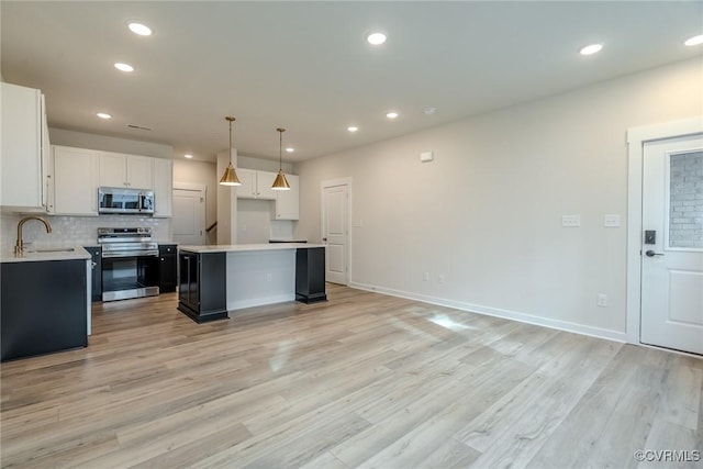 kitchen with sink, hanging light fixtures, appliances with stainless steel finishes, a kitchen island, and white cabinetry