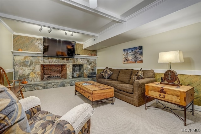 carpeted living room with track lighting, a stone fireplace, beam ceiling, wooden walls, and crown molding