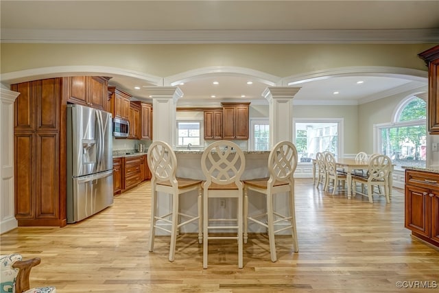 kitchen featuring light stone countertops, ornate columns, light hardwood / wood-style floors, stainless steel appliances, and crown molding