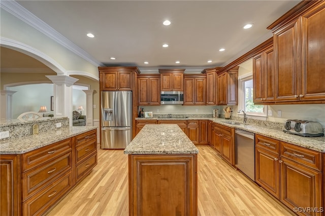 kitchen with light wood-type flooring, stainless steel appliances, sink, ornate columns, and a center island