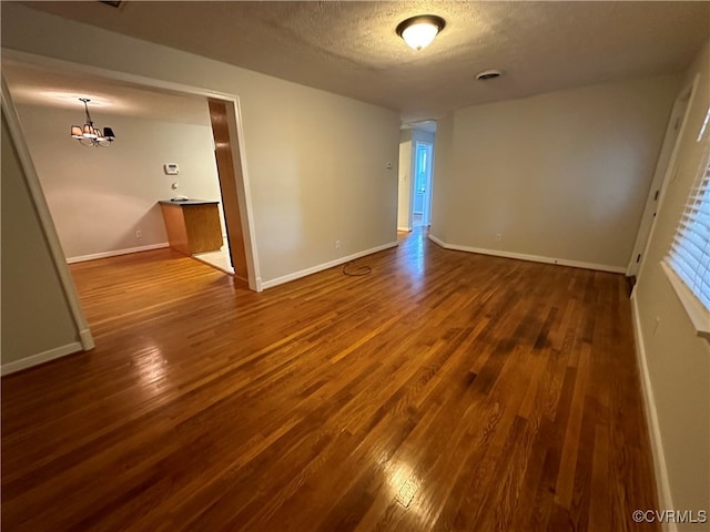 unfurnished room with a notable chandelier, dark wood-type flooring, and a textured ceiling