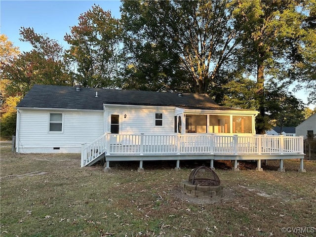 back of property featuring a deck, a fire pit, a sunroom, and a yard