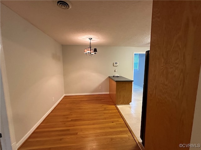 unfurnished dining area with a textured ceiling, light hardwood / wood-style floors, and a notable chandelier