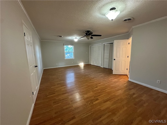 unfurnished bedroom with hardwood / wood-style flooring, a textured ceiling, two closets, ceiling fan, and ornamental molding