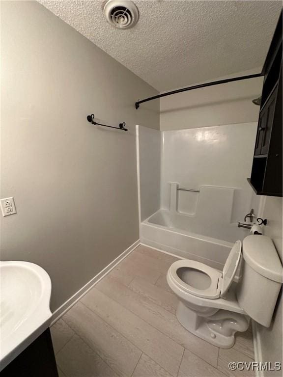 full bathroom featuring toilet, a textured ceiling, washtub / shower combination, and sink