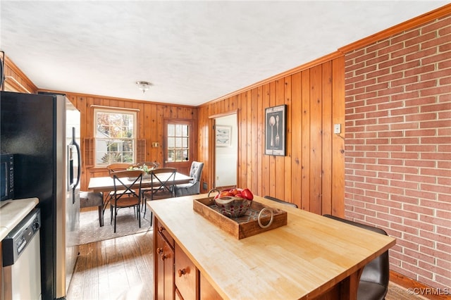 kitchen with stainless steel appliances, wooden walls, crown molding, hardwood / wood-style flooring, and butcher block countertops